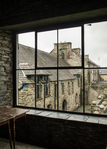 A dark stone room with a window overlooking the courtyard of a building.