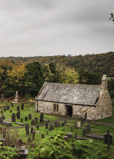 A church and graveyard with a suspension bridge in the background.