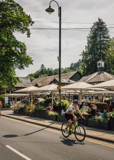 A group of cyclists on a road passing shops in a village.