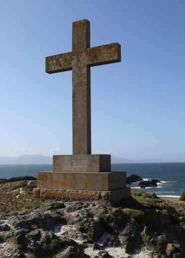 A cross with the coastline and lighthouses in the distance.