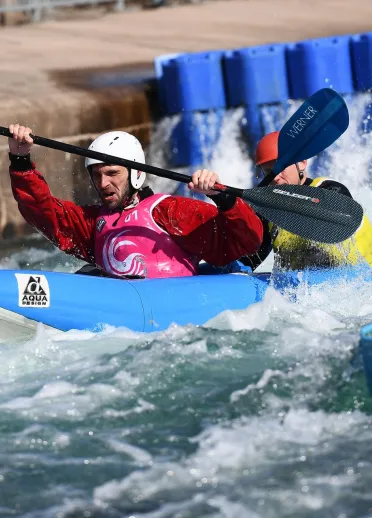Two men in a kayak paddling on the rapids in a sports village.