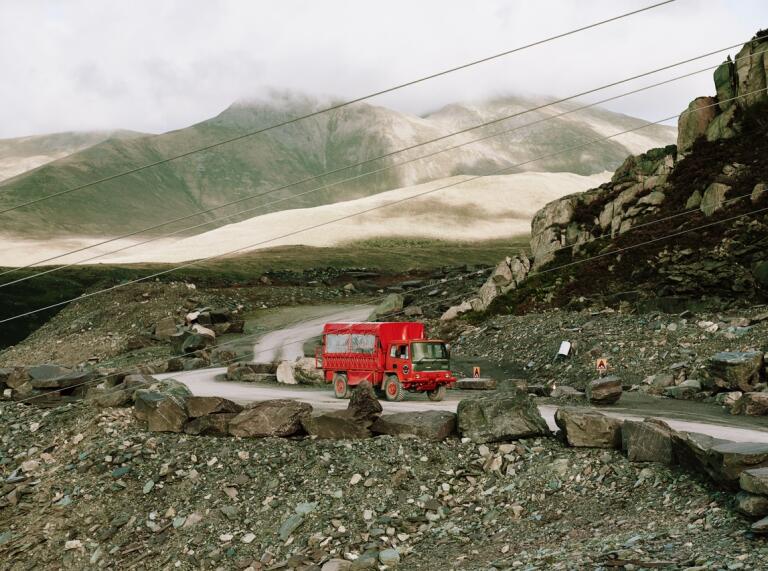 A red touring truck driving through a quarry.