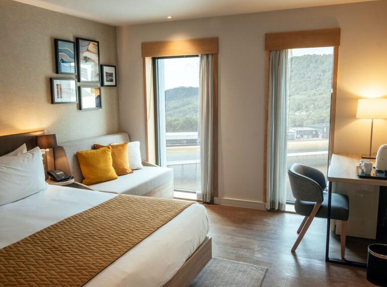 A bedroom at a hotel with views of a surf lagoon out the windows.