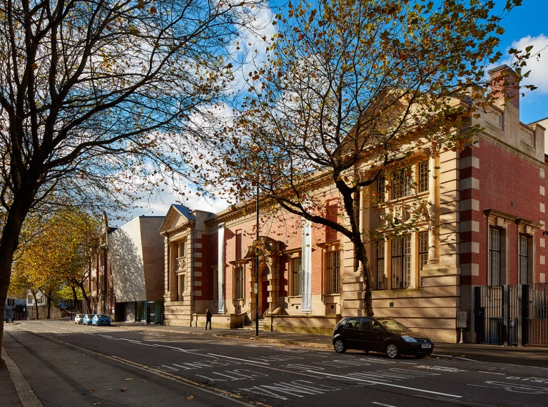 A red and sand brick building, home to an art gallery on a tree lined road.