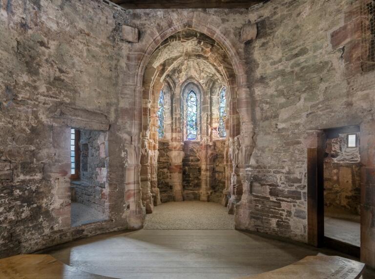 Inside a castle with entrances and an archway with stained glass windows.