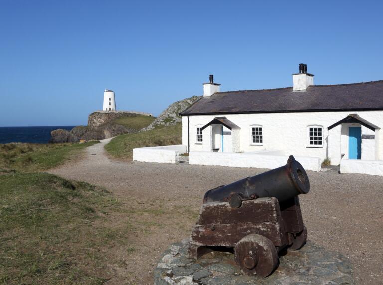 A lighthouse, white house and cannon on an island.