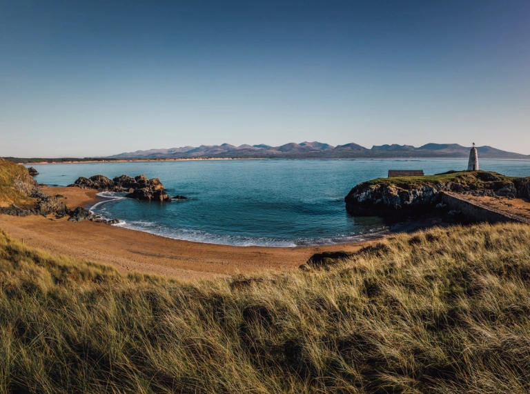 A cove with a golden beach and a lighthouse on the headland.