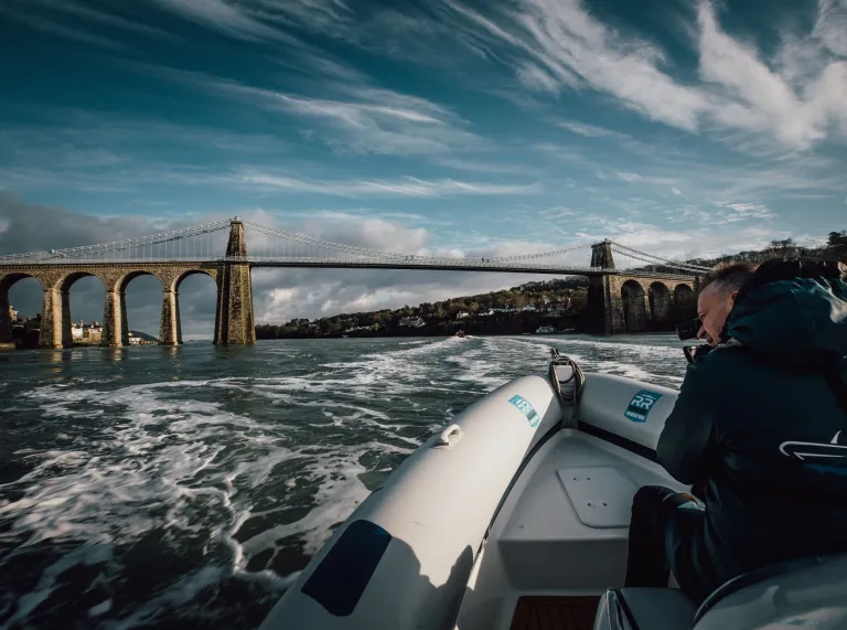 A speedboat on the strait travelling toward a large bridge.