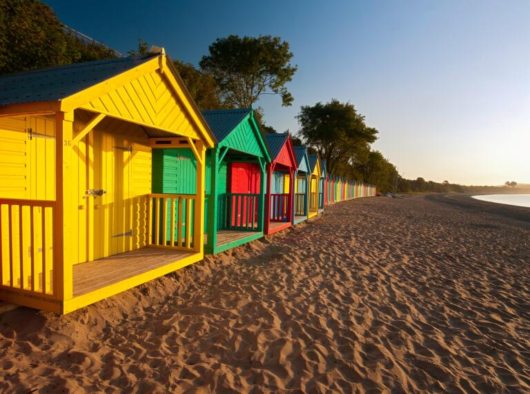 A row of colourful beach huts as the sun sets.