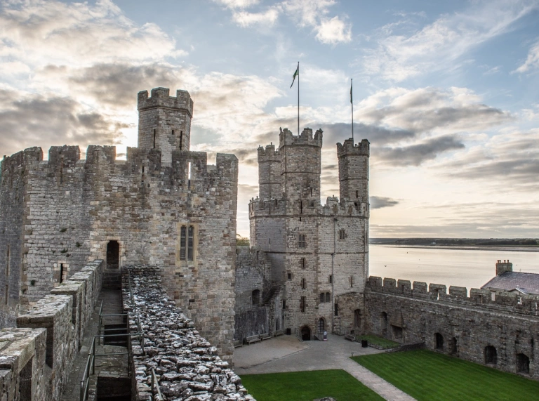 View of the turrets of a preserved castle from the courtyard with the sea beyond.