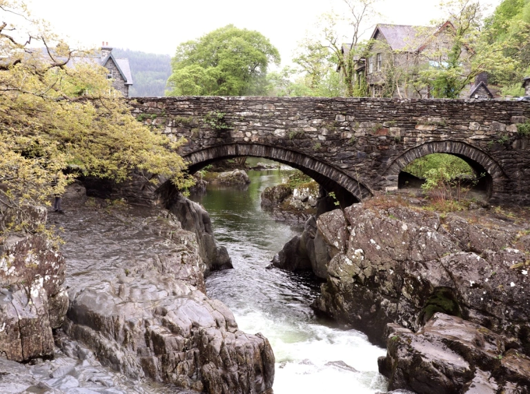 A river running through a stone bridge between rock formations in a pretty village.