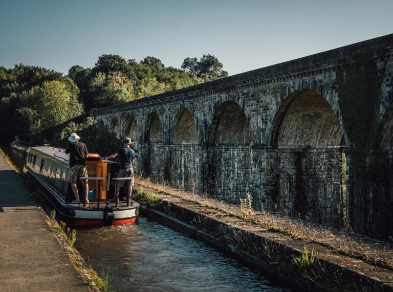 A narrowboat travelling alongside an aqueduct on a canal.