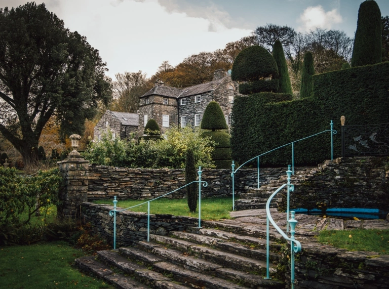 A garden with a staircase, ornate hedges and a grand house.