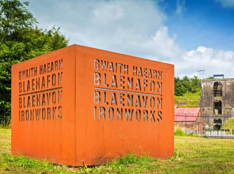 A viaduct behind a wrought iron cube etched with the words Blaenavon Ironworks.