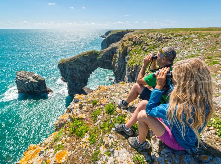 A couple on the coast path looking out to sea with binoculars.