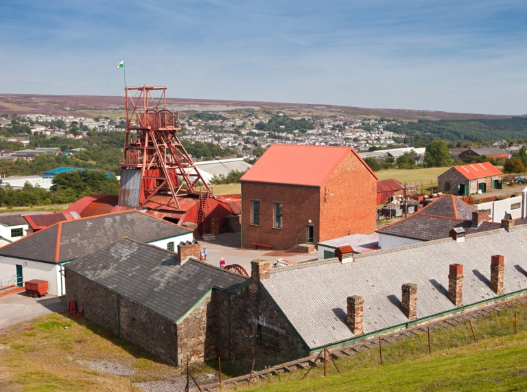 Colliery buildings and a pit head overlooking a town in the South Wales valleys.