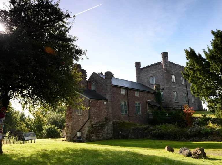 A castle surrounded by lush green grass blue sky, with the sun streaming through the tree.