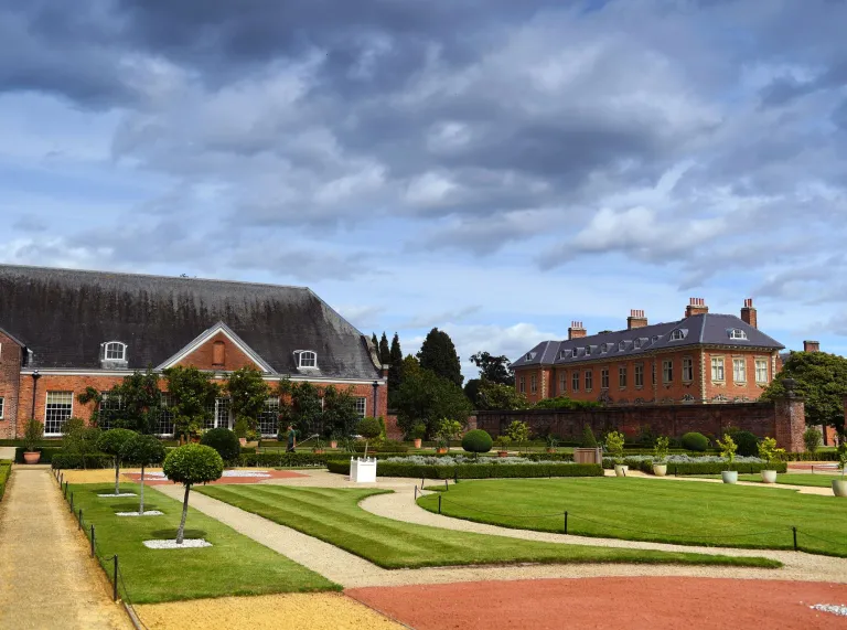 Lawned gardens, footpaths and trimmed topiary outside a grand house.