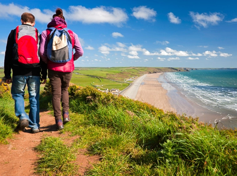 Walkers on the coast path heading toward a beach.