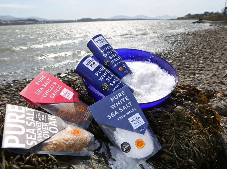 A range of Halen Môn sea salt products displayed on the coast against the tide.