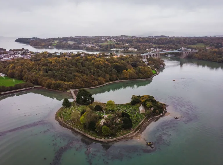 An aerial shot of a small island with a suspension bridge across the strait.