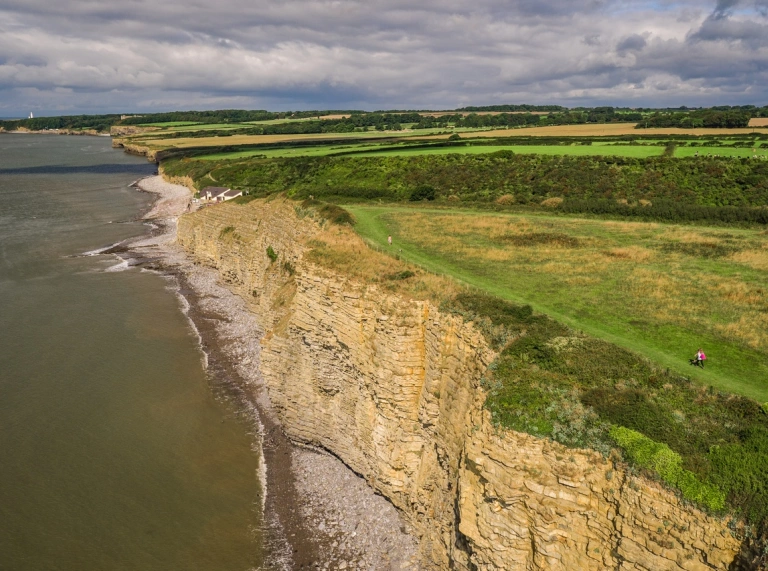 People walking along the Wales Coast Path showing dramatic cliffs and shorline.