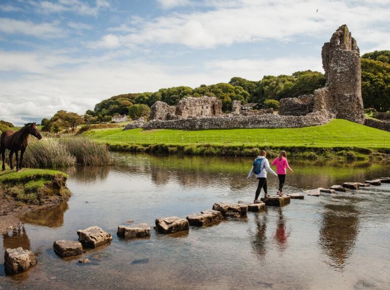 People walking on stepping stones over an estuary toward a castle.