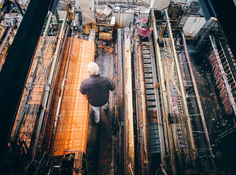 A man standing amongst working weaving machines.