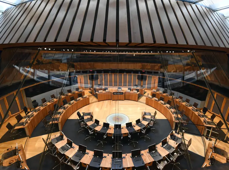 Chairs and tables set in a circle inf the debating chamber of a parliament building.
