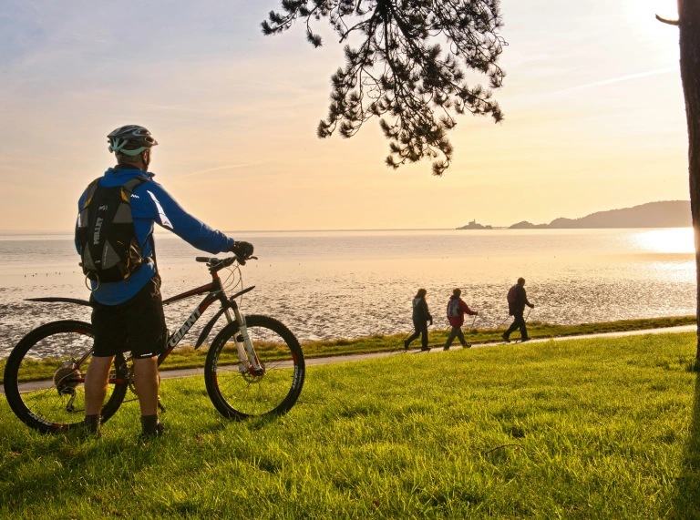 Cyclists on Coast Path at Blackpill at sunrise with Mumbles Head in background