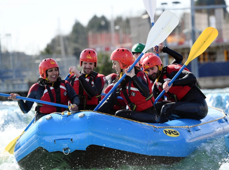 A group of people wearing helmets, wetsuits and life jackets in a white water rafting boat.