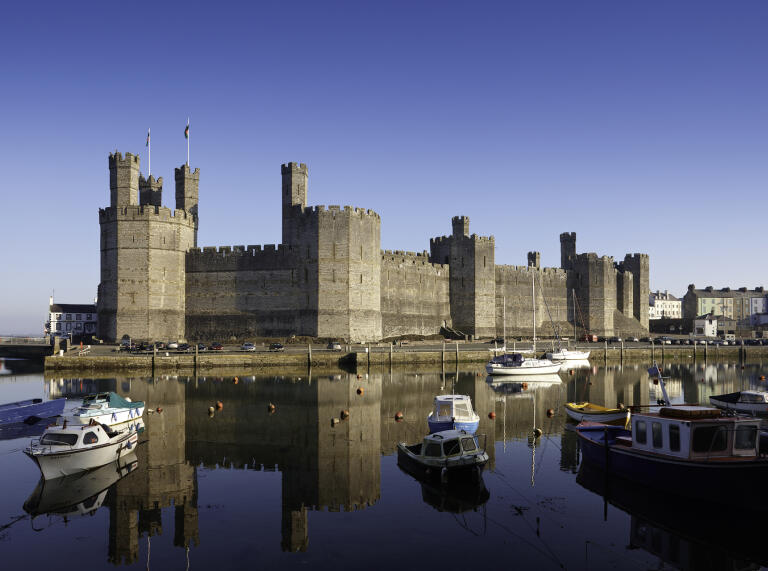 An exterior shot of Caernarfon Castle behind the estuary filled with boats.