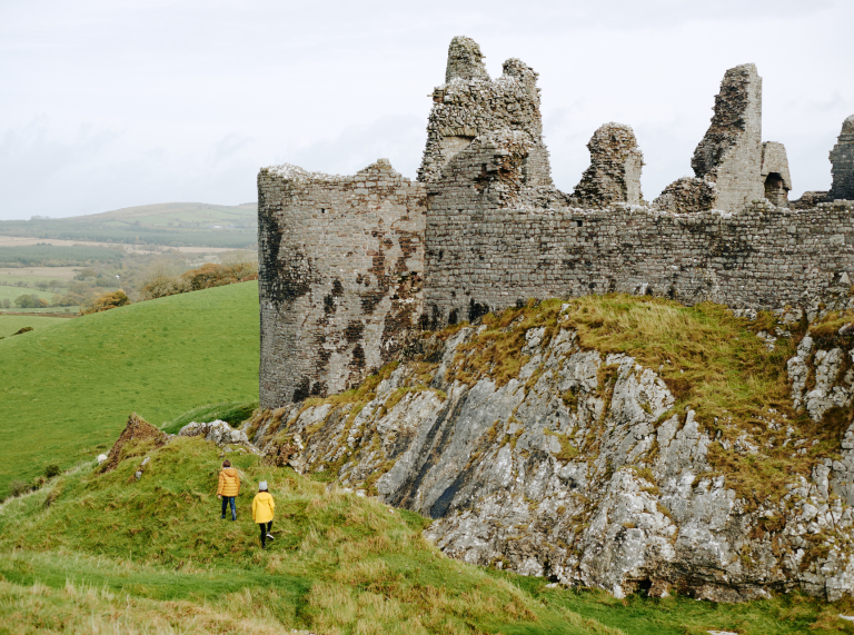 Two people exploring external stone walls of Carreg Cennen Castle.