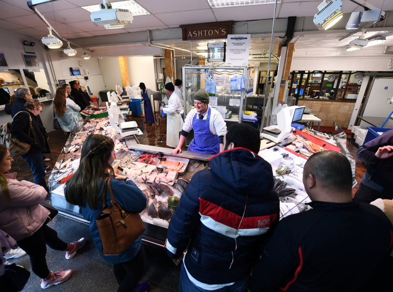 A group of people looking at the large selection of fish at Cardiff Market.