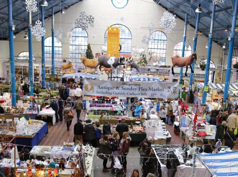View of indoor market stalls and shoppers from above with models of farm animals hanging down.