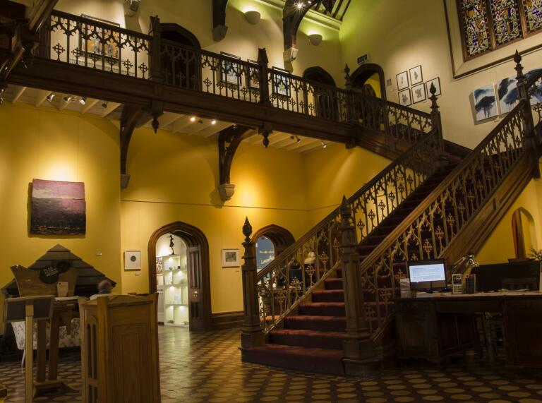Grand staircase and landing in in Plas Glyn-y-Weddw art gallery with art on the walls.