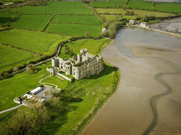 Aerial shot of Carew Castle alongside a river and green fields.
