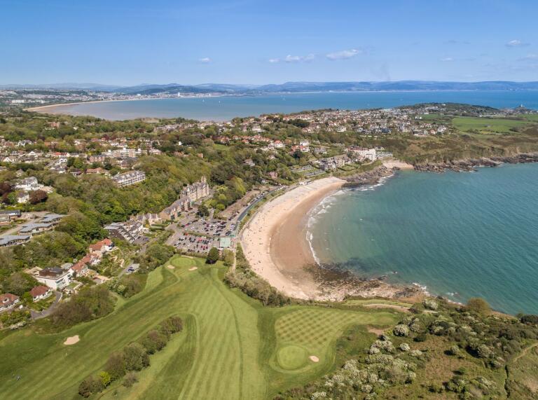 Aerial shot of a golf course and coastline in the sunshine.