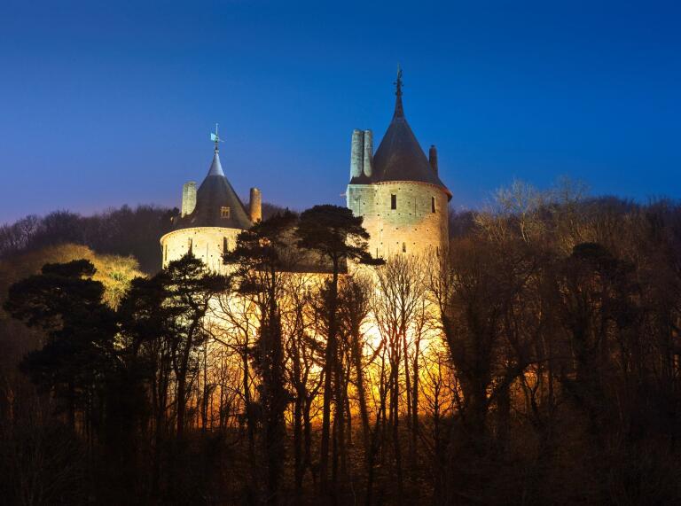 Castell Coch illuminated at night framed by the silhouette of trees in the darkness.