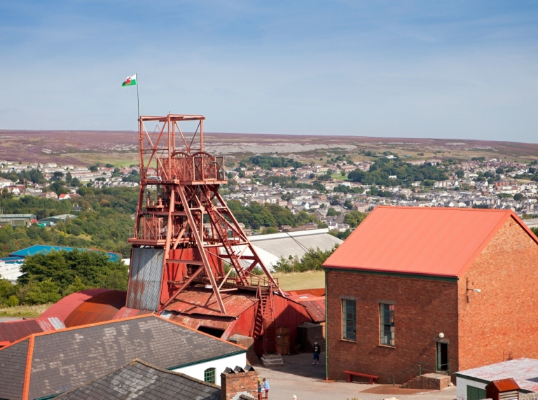 A view of a forecourt with a red pit wheel and a red building in Blaenavon.