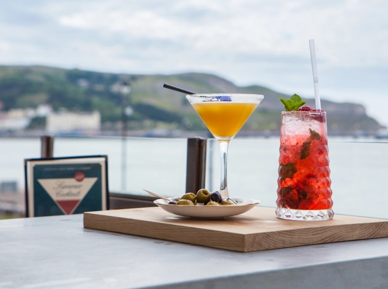 olives and drinks on table with blurred coast view.