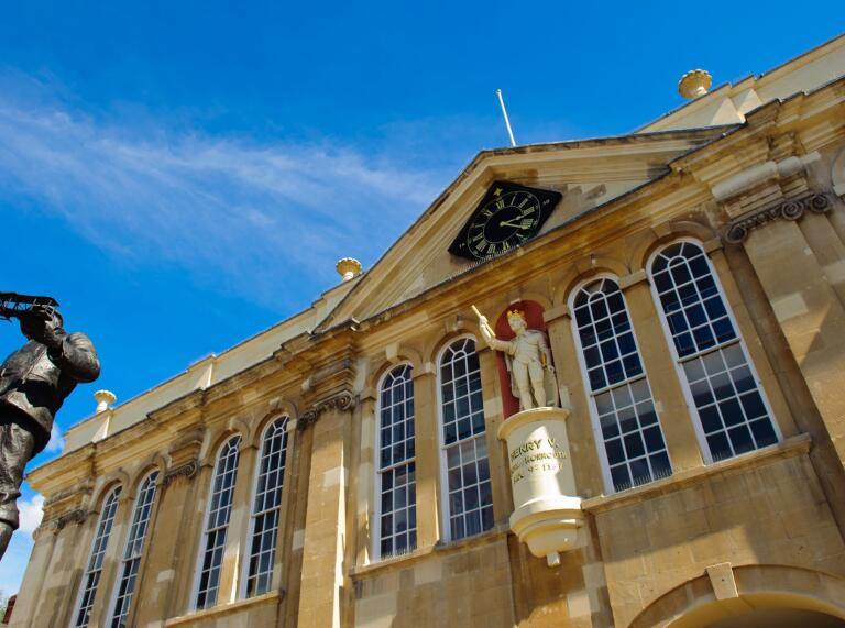 A town hall with large windows displaying a statue of Henry V and a clock.