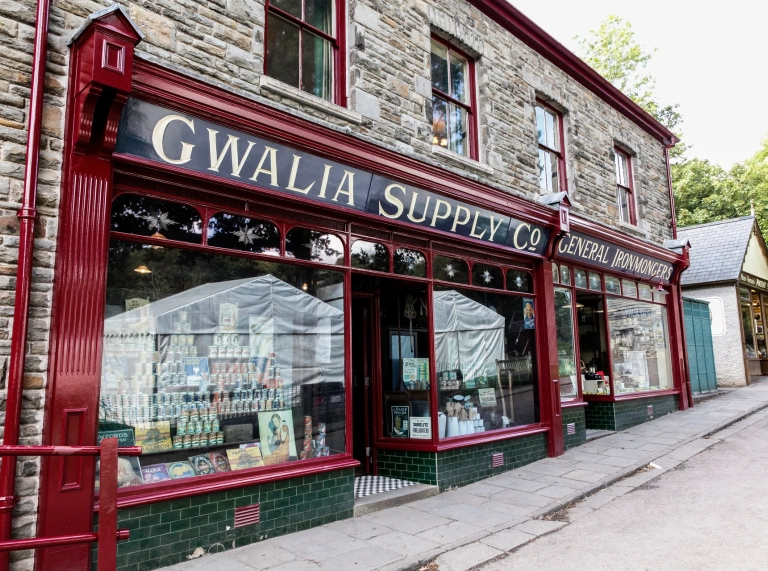 Exterior of a food store and ironmonger with displays in windows.