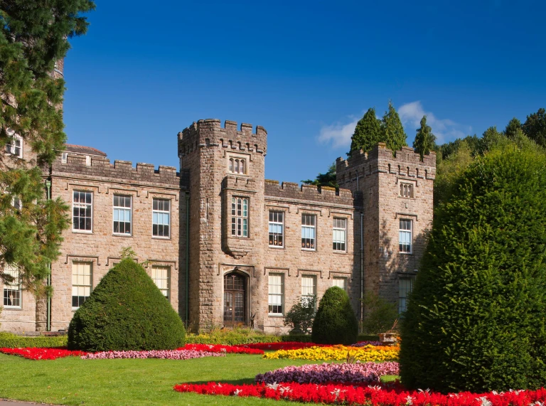 A castle-style building with towers and many windows and a colourful garden.