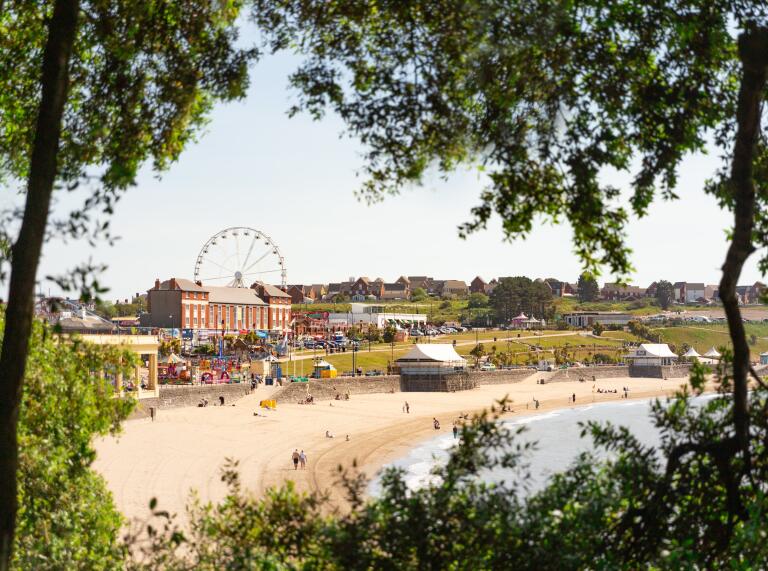 Beach and funfair viewed from distance through trees.