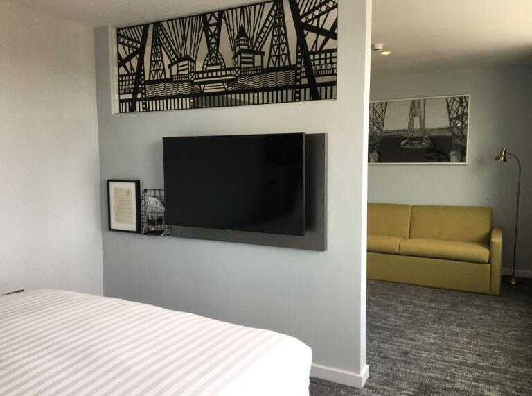 A hotel room showing a bed, tv and settee, with images of a transporter bridge.