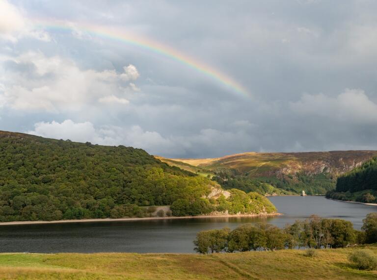 Rainbow over a reservoir in a valley surrounded by mountainous landscape.