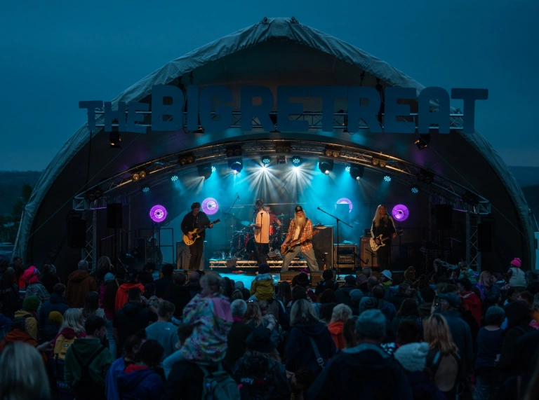 A rock band playing on an outdoor stage in front of a crowd.