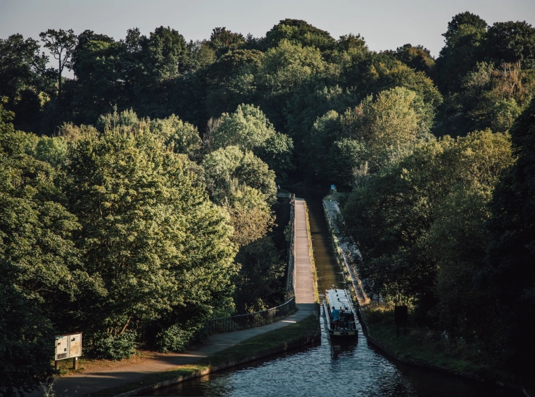 A narrowboat on a canal heading toward a viaduct.