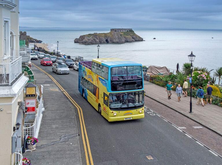 An open top bus driving along the coastline